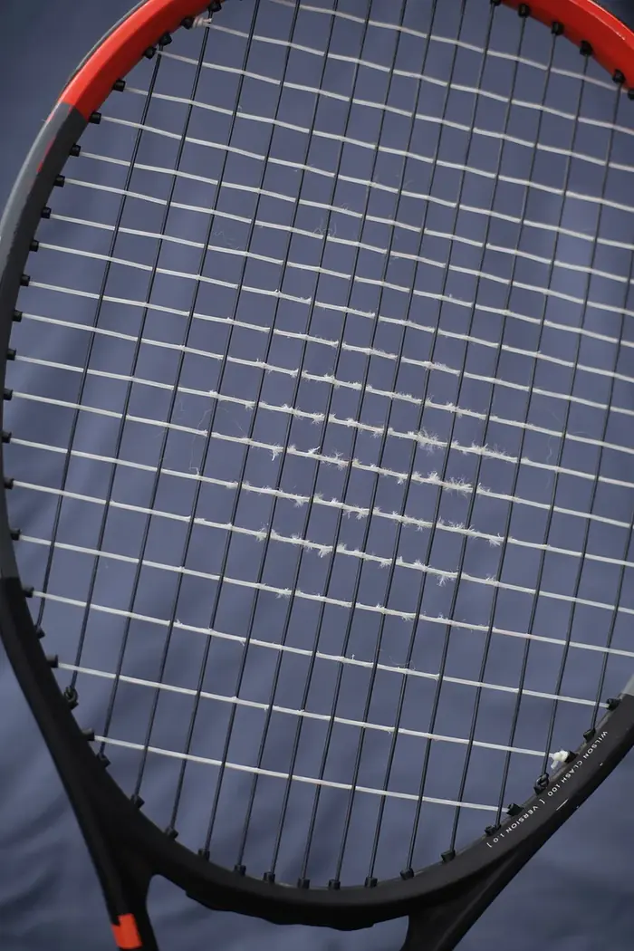 Yakından çekilmiş, telleri çentiklenmiş ve aşınmış bir tenis raketi kordajı