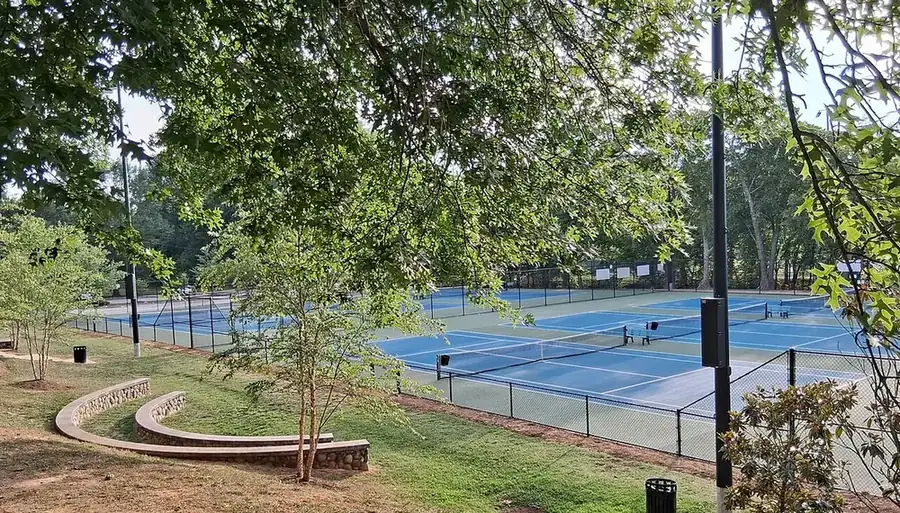 Ağaçlarla çevrili, mavi-yeşil zeminli sert tenis kortları