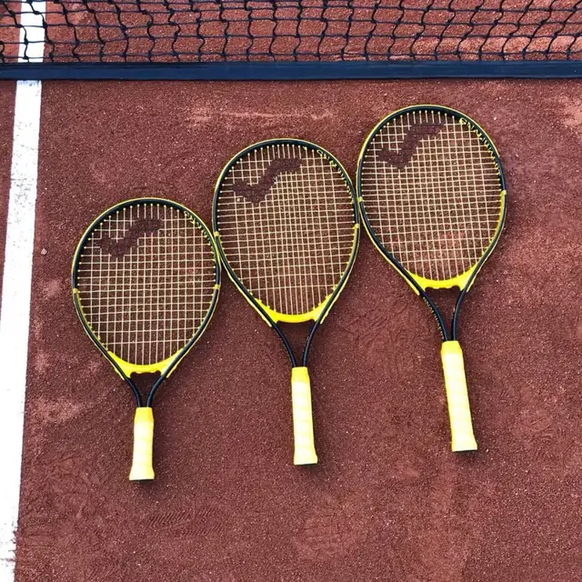 Farklı boylarda üç çocuk tenis raketi toprak kortta yan yana